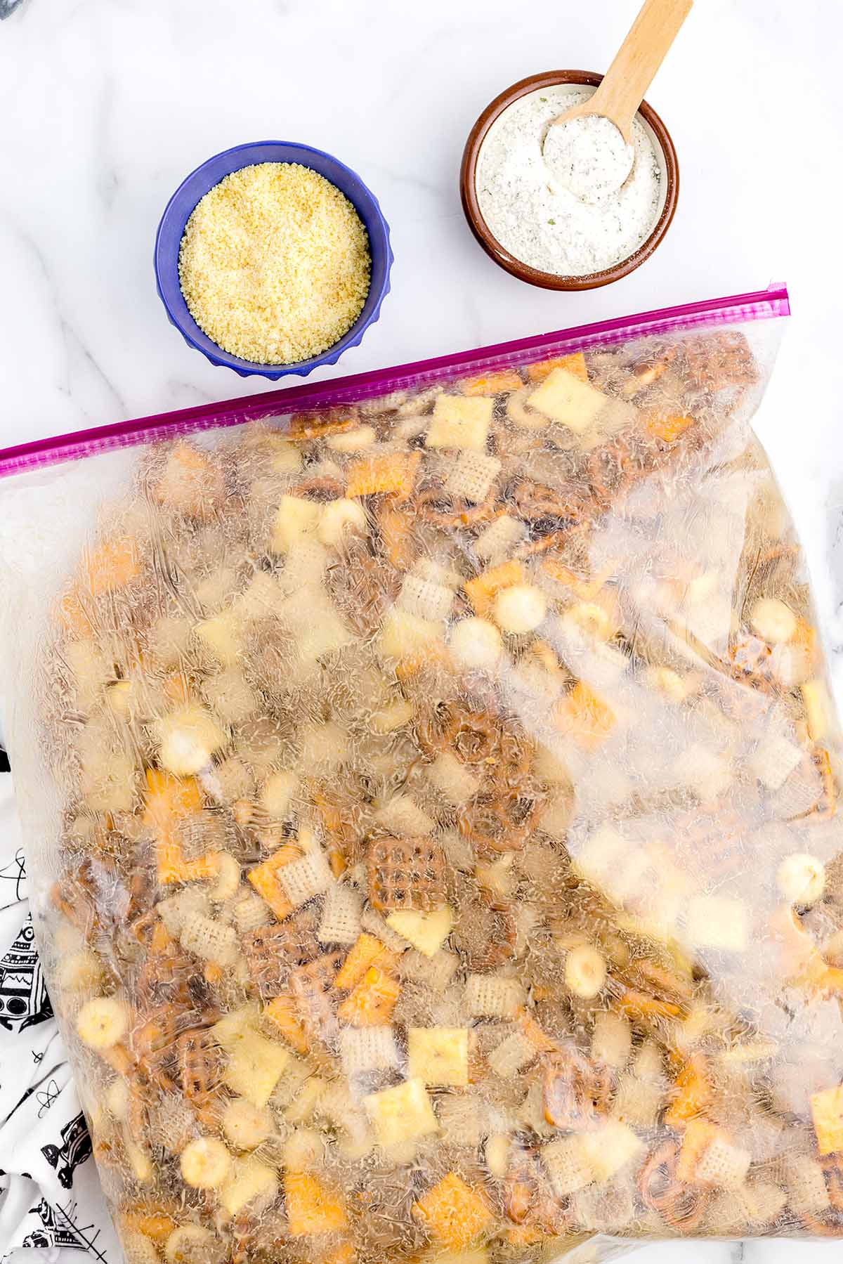 Ranch Chex Mix with cereal, pretzels, crackers, and nuts being seasoned in a large plastic bag.