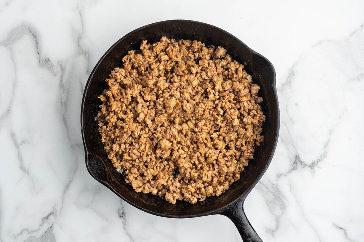 Seasoned ground chicken cooking in a skillet for Asian chicken lettuce wraps.