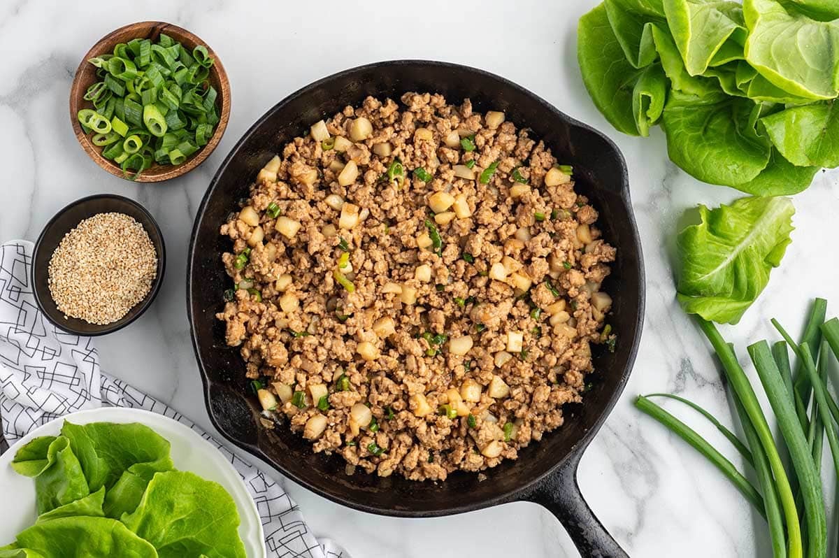 Asian chicken lettuce wrap filling with ground chicken, water chestnuts, and green onions in a skillet.