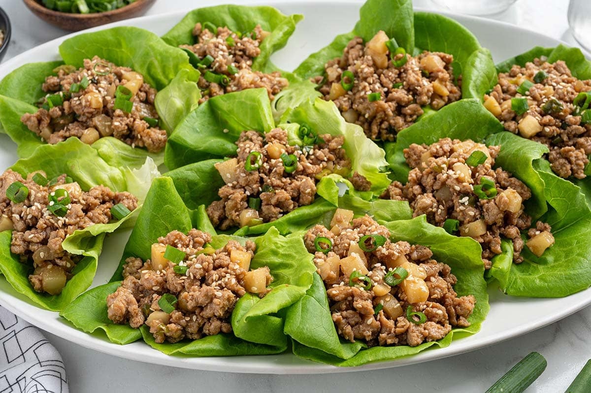 Asian chicken lettuce wraps with ground chicken, water chestnuts, green onions, and sesame seeds on a platter.