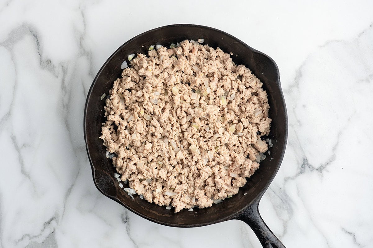 Ground chicken and diced onions cooking in a skillet for Asian chicken lettuce wraps.