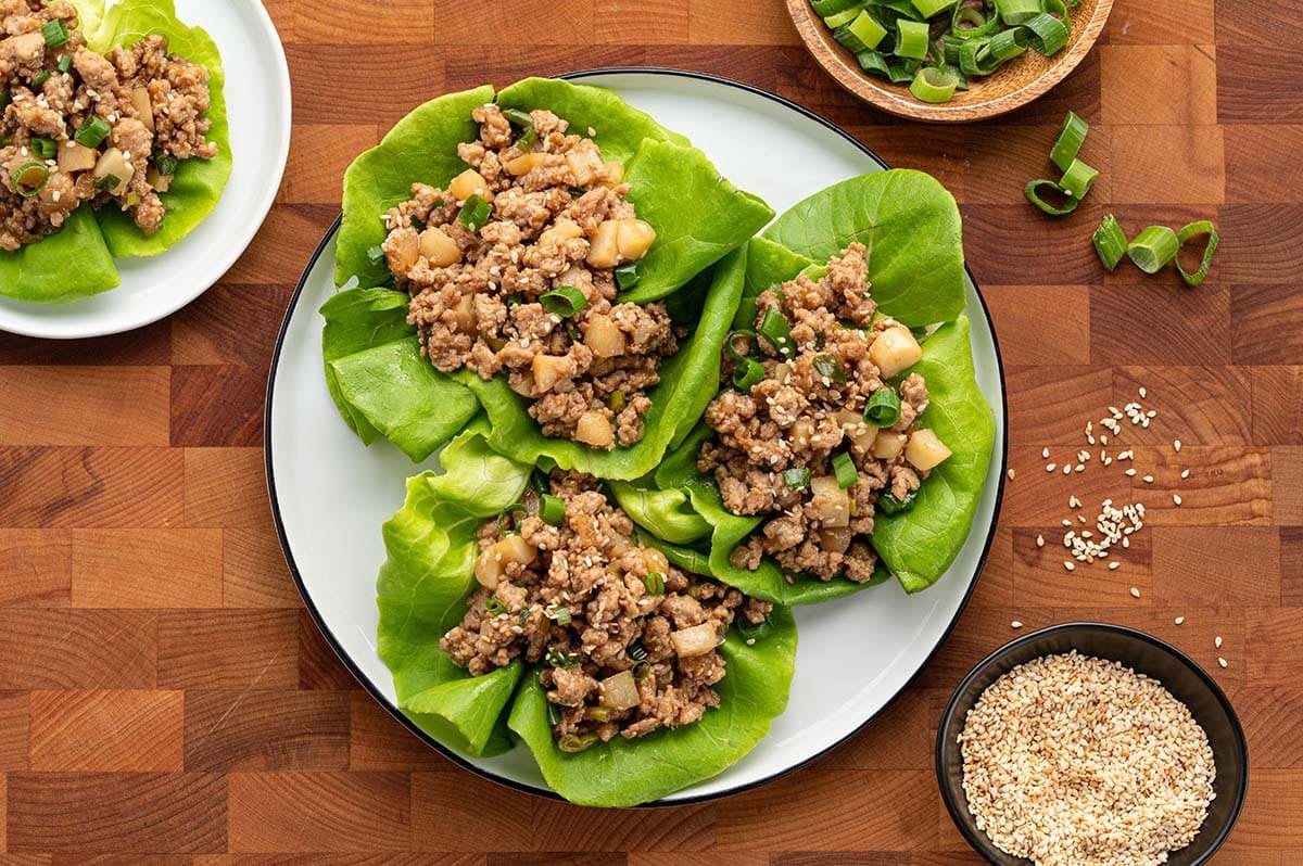 Asian chicken lettuce wraps with ground chicken, water chestnuts, green onions, and sesame seeds on a plate.