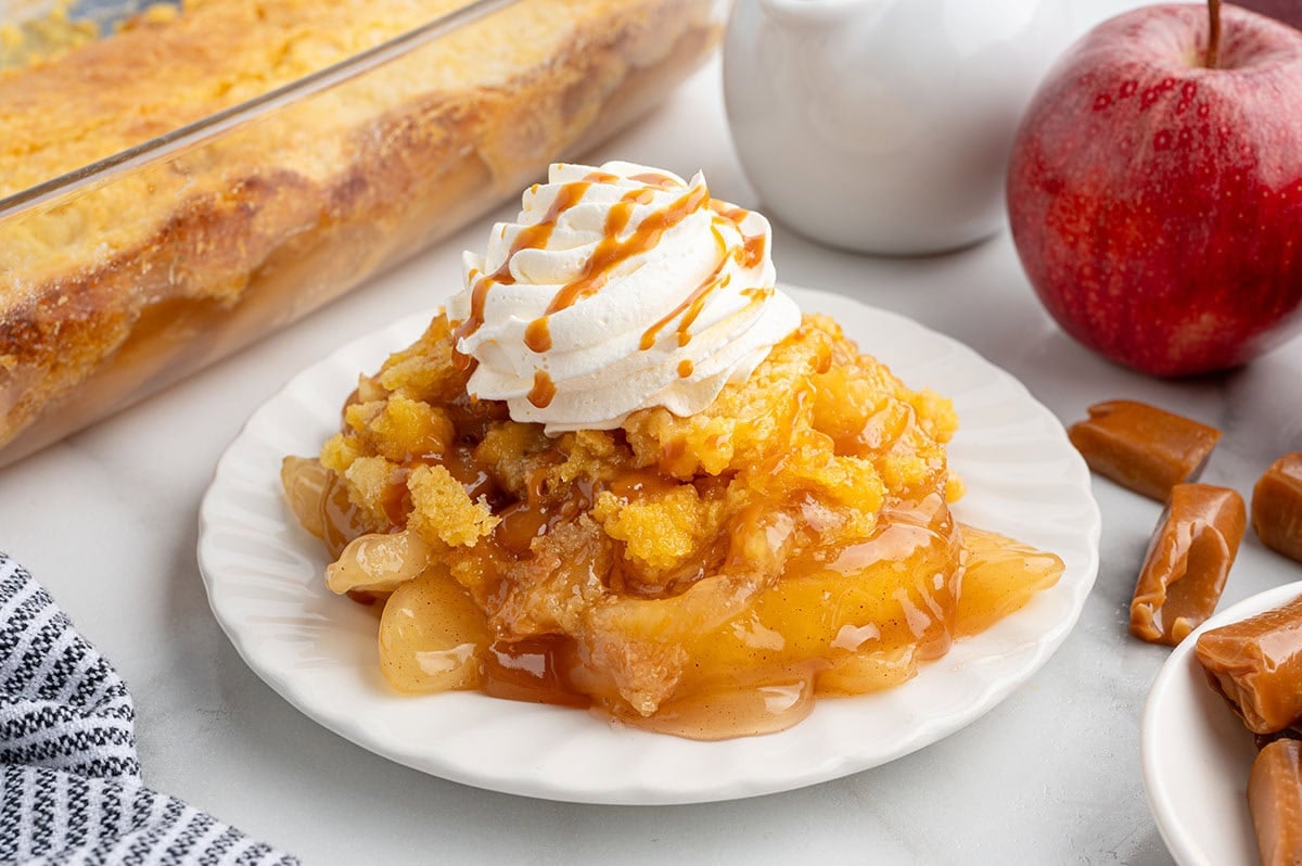 Caramel apple dump cake topped with whipped cream and caramel drizzle on a plate.