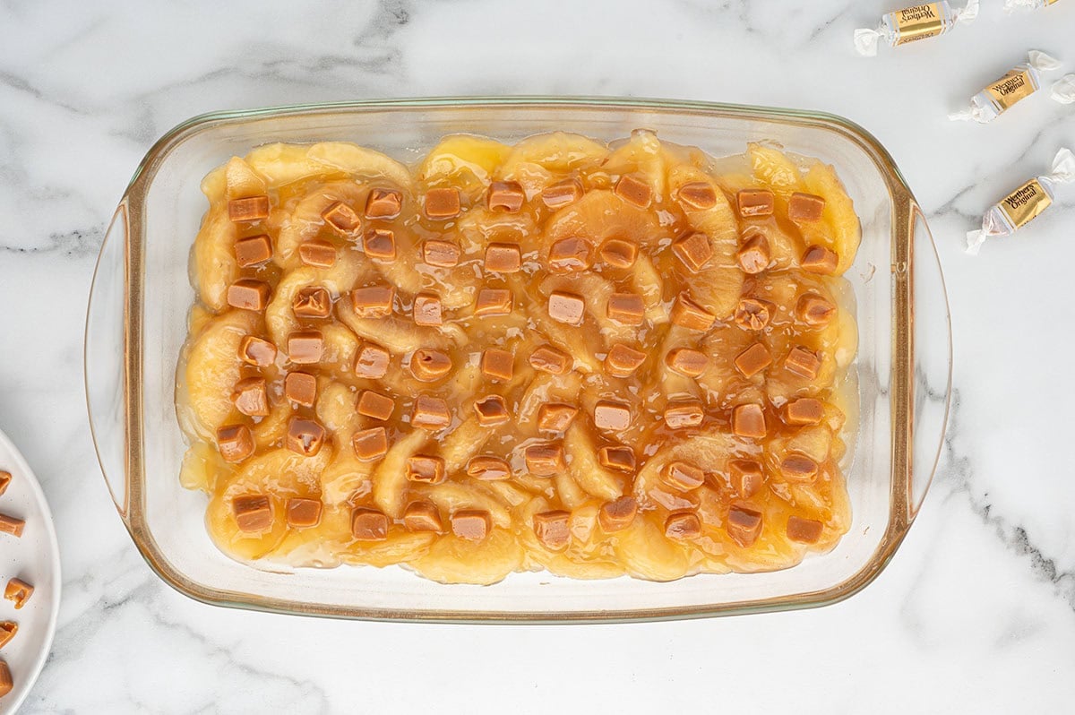 Caramel bits scattered over sliced apples in a glass baking dish.