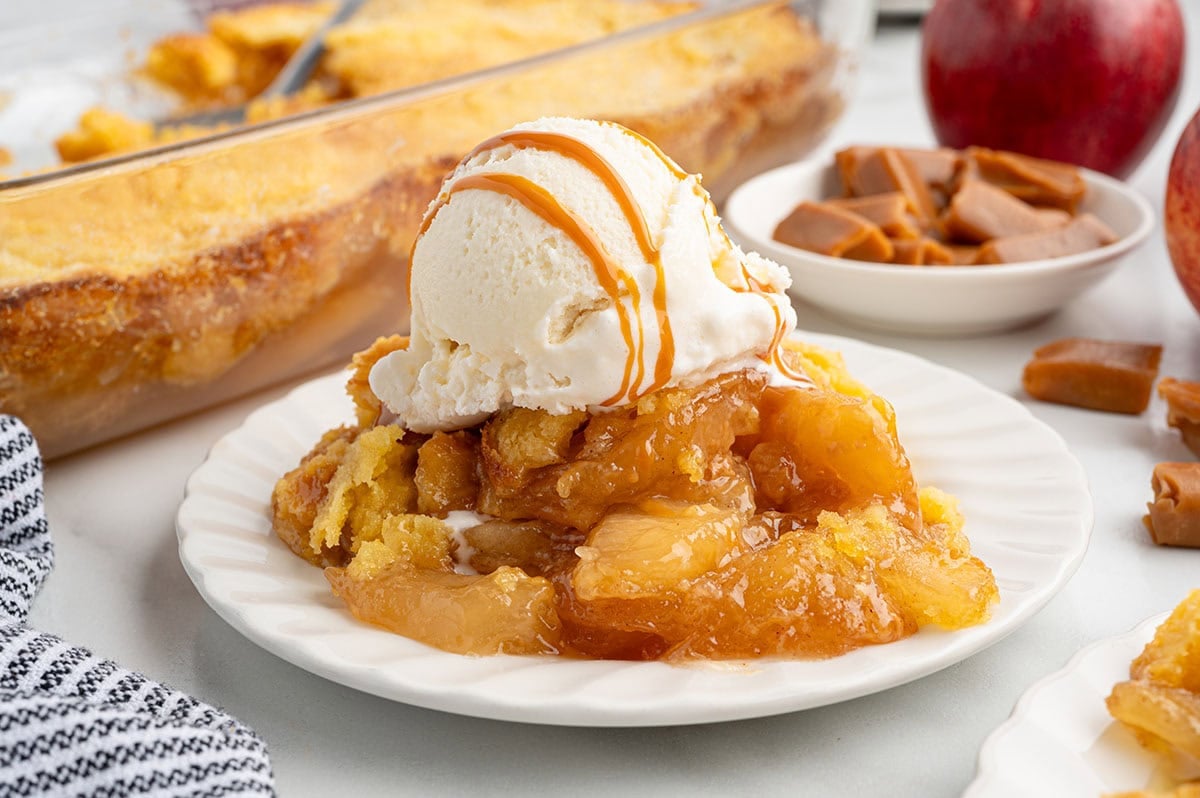 Caramel apple dump cake topped with vanilla ice cream and caramel drizzle on a plate.