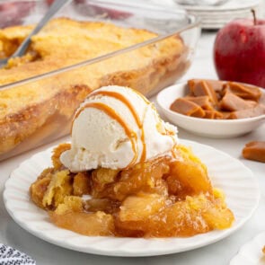 Plated caramel apple dump cake with vanilla ice cream and caramel drizzle, baking dish in background.