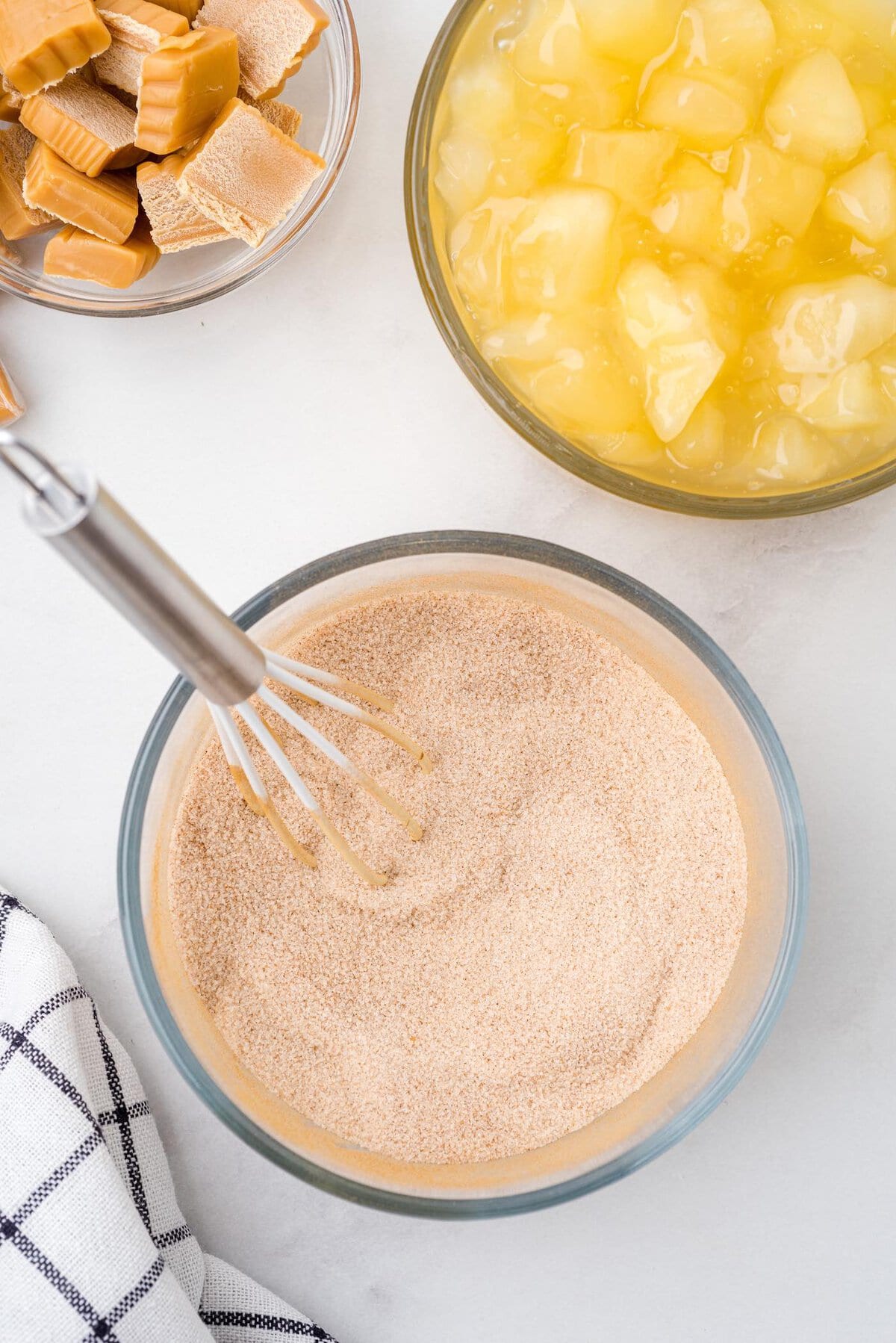Cinnamon sugar being whisked in a bowl next to caramel candies and apple pie filling