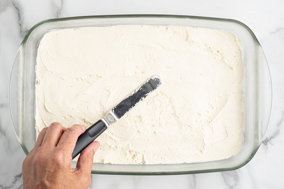 Hand spreading cream cheese filling over the crust with an offset spatula.