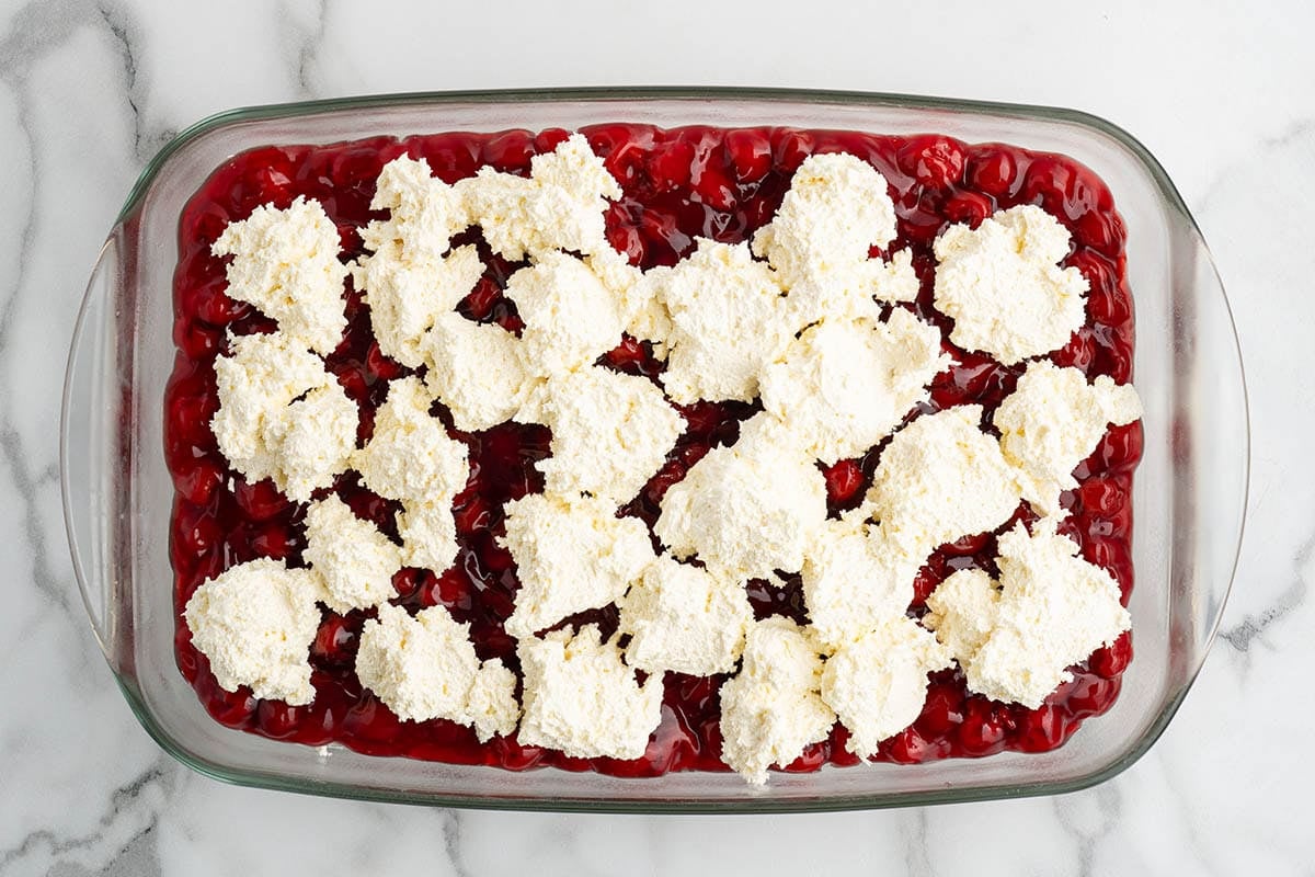 Dollops of whipped topping over cherry pie filling in a baking dish.