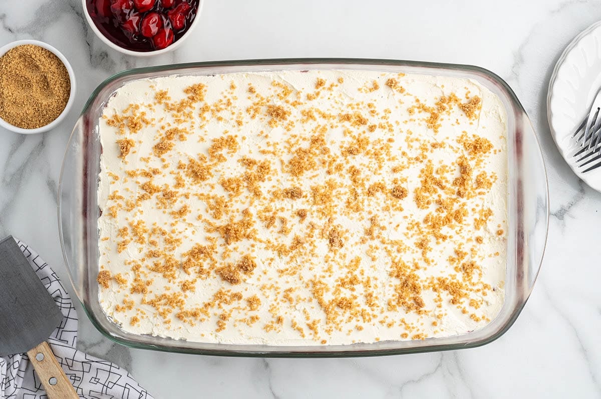 Assembled cherry yum yum dessert topped with graham cracker crumbs, ready to chill.