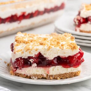 Slice of layered cherry yum yum dessert with graham cracker crust and cream layers.