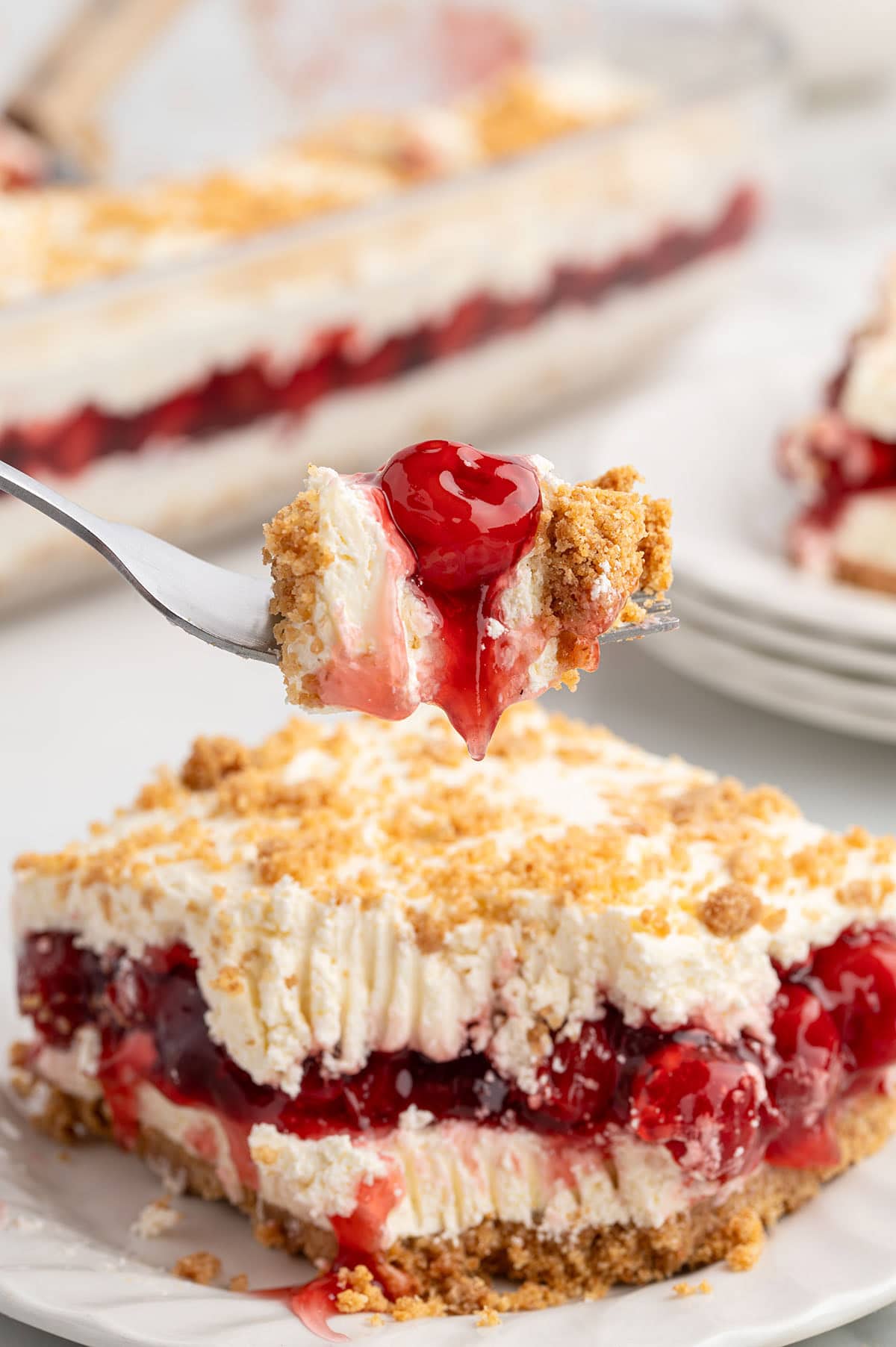 Fork lifting a bite of cherry yum yum dessert with a slice on a plate below.