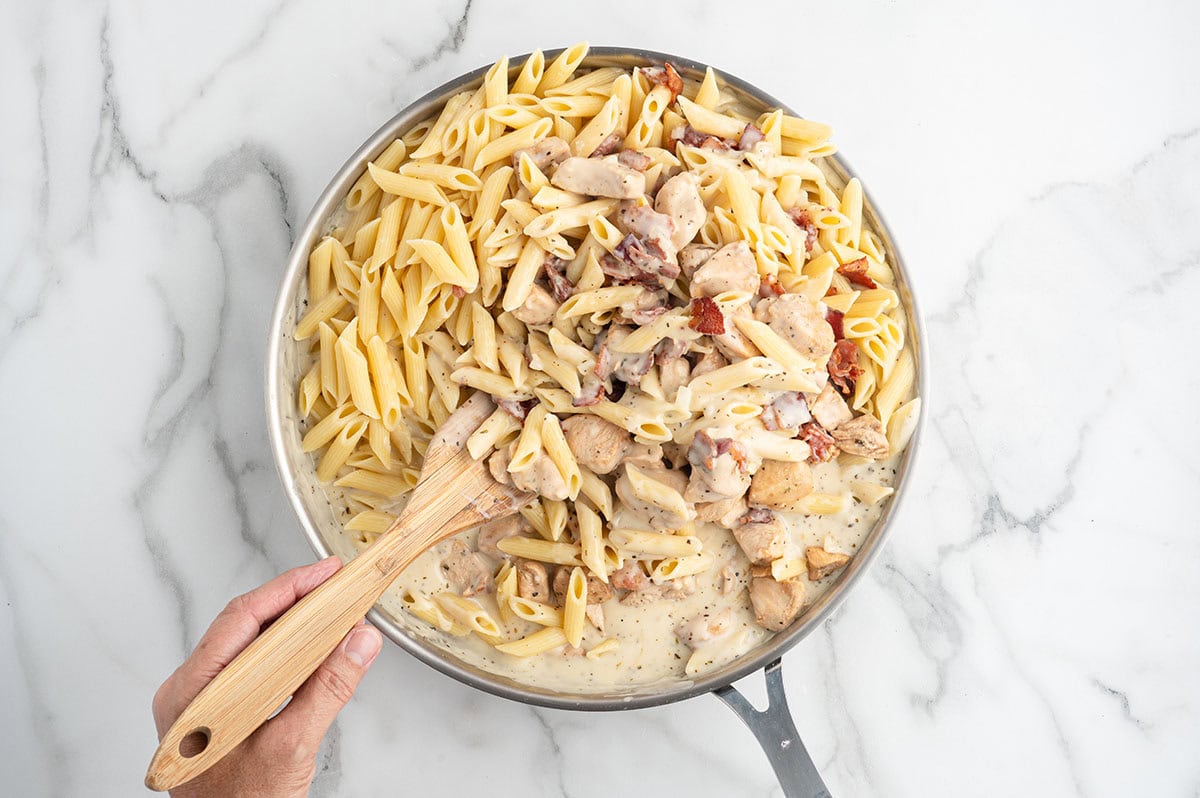 Add the cooked penne, chicken, and crispy bacon to the creamy ranch sauce, then stir until everything is evenly coated.