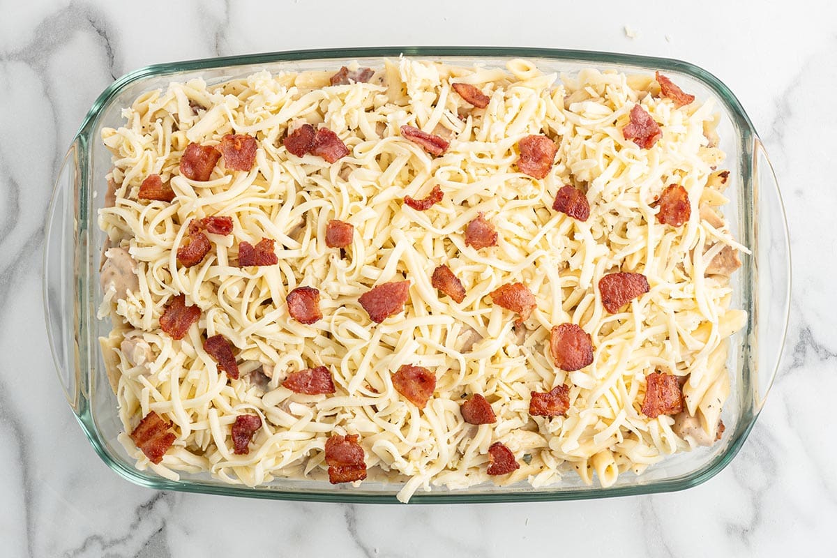 Transfer the creamy chicken and pasta mixture to a baking dish, then top evenly with shredded cheese and the remaining crispy bacon.