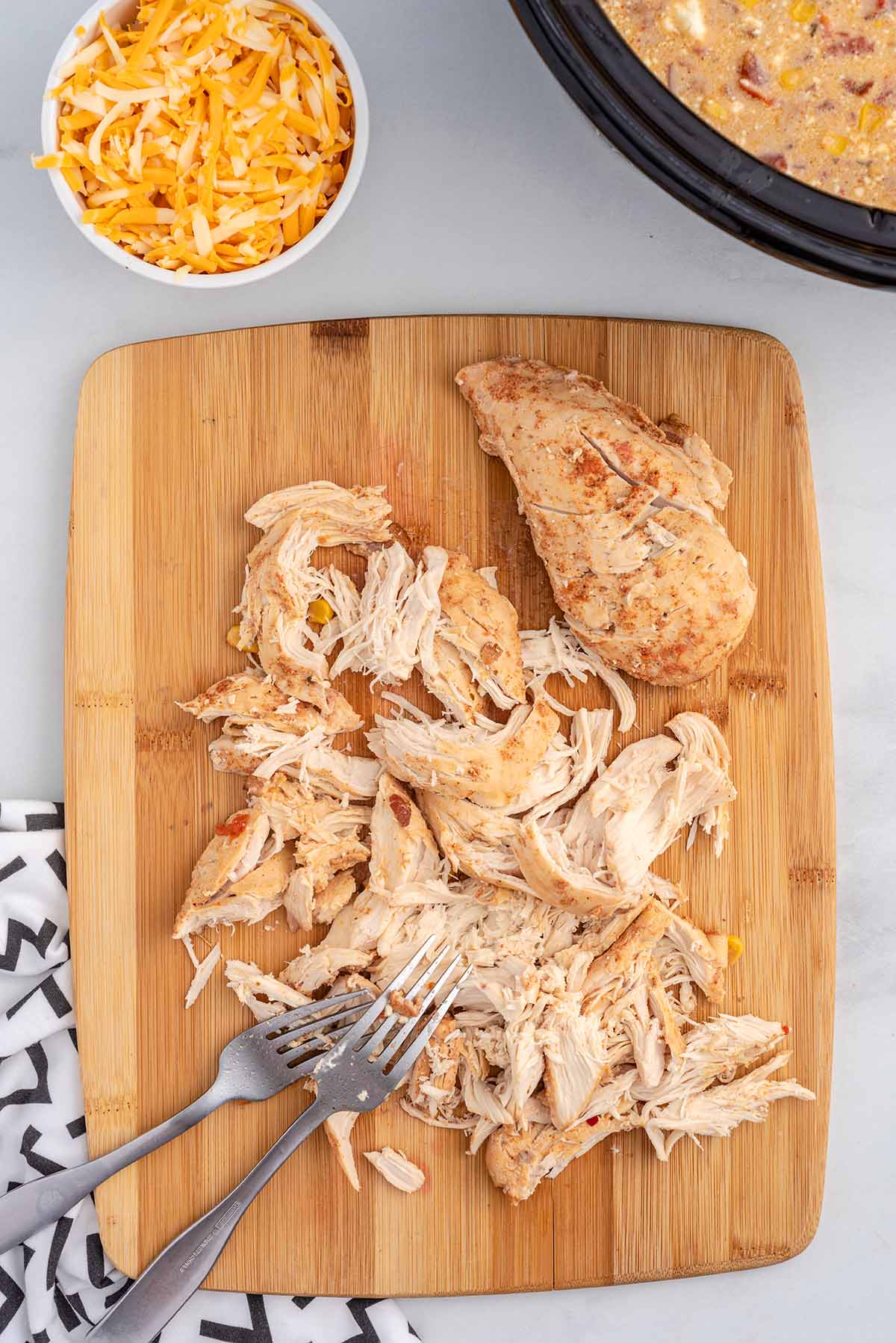 Shredded chicken for crack chicken chili on a cutting board with two forks.