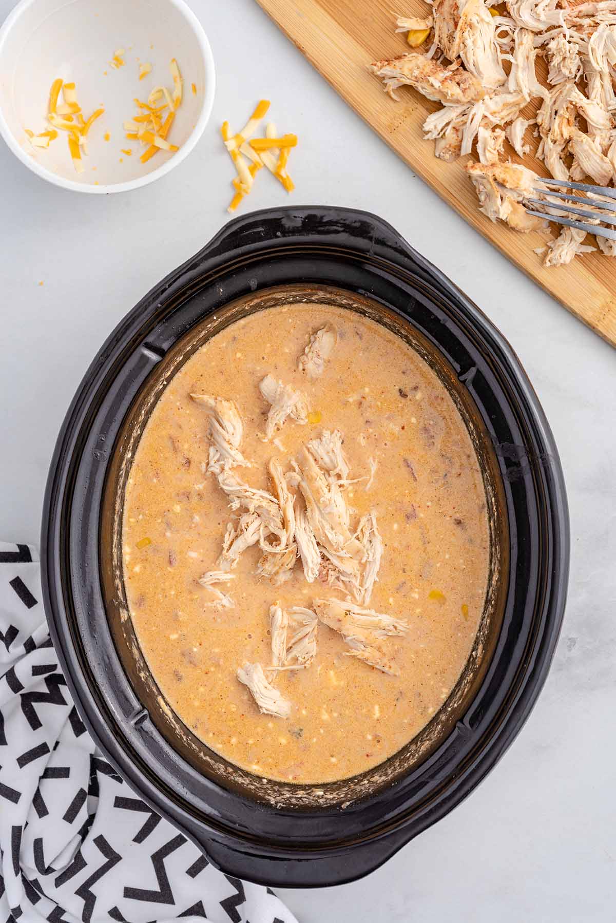 Shredded chicken being added to creamy crack chicken chili in a slow cooker.