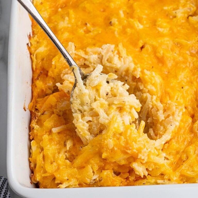 Spoon scooping cheesy hashbrown casserole from a white baking dish.