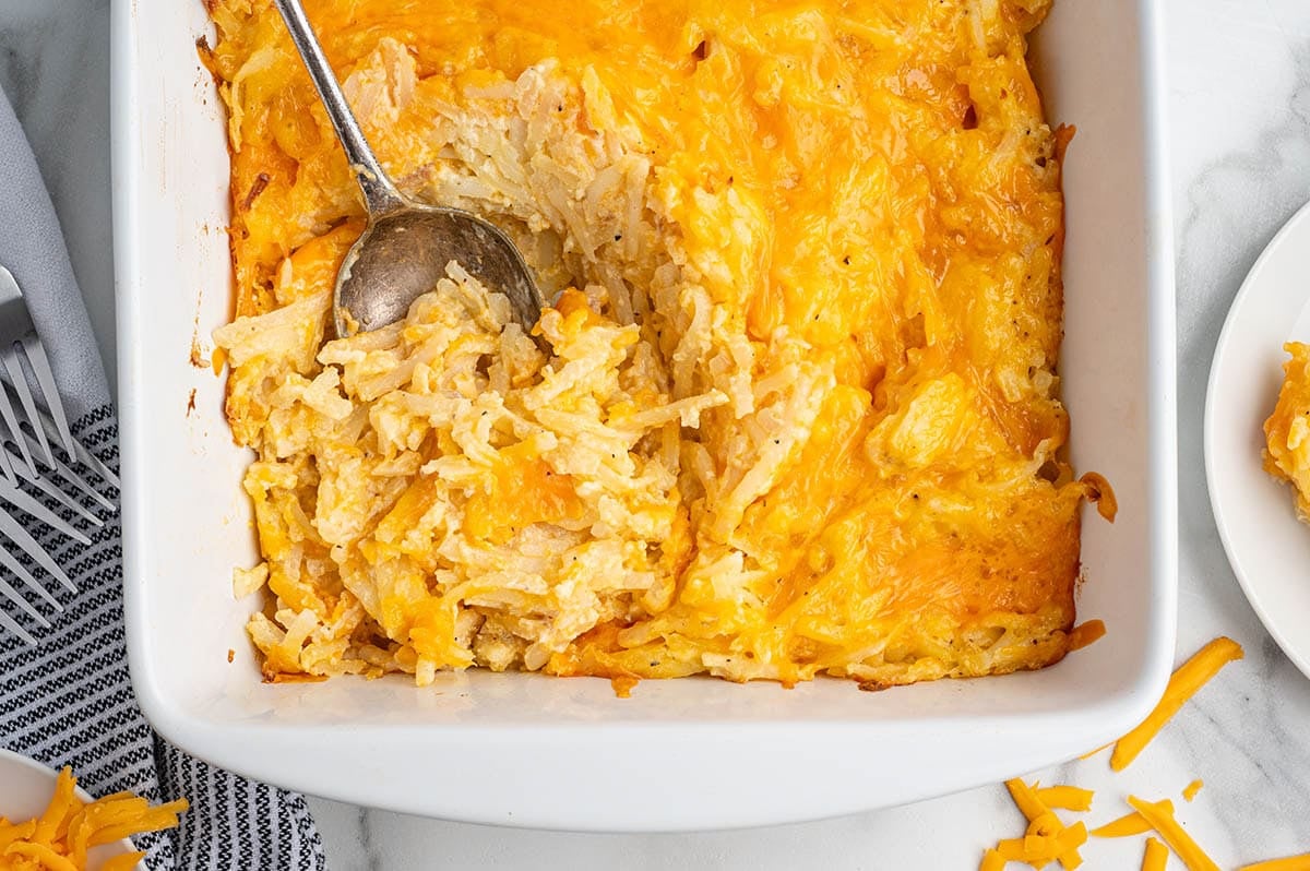 Overhead view of cheesy hashbrown casserole in a white dish with a serving spoon.