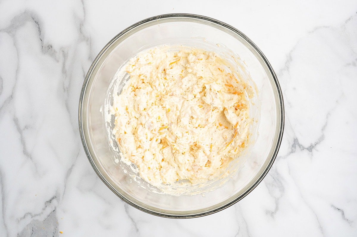 Hashbrown casserole ingredients mixed together in a glass bowl before baking.