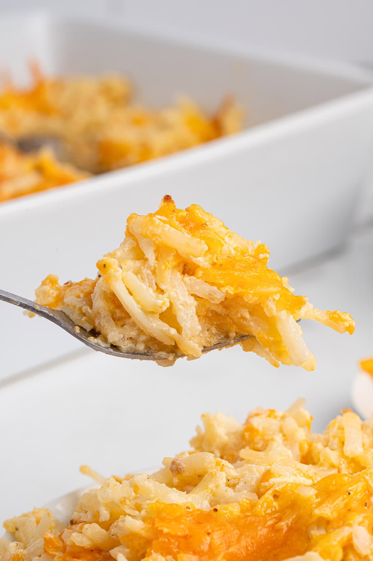 Forkful of cheesy hashbrown casserole held above the baking dish.