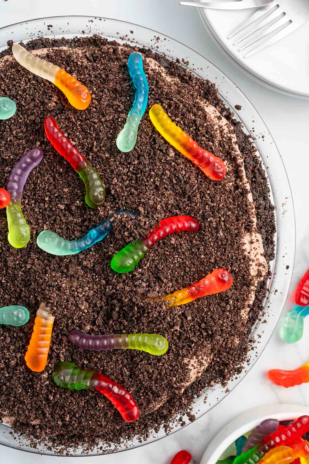 Overhead view of dirt pie topped with crushed Oreos and colorful gummy worms.