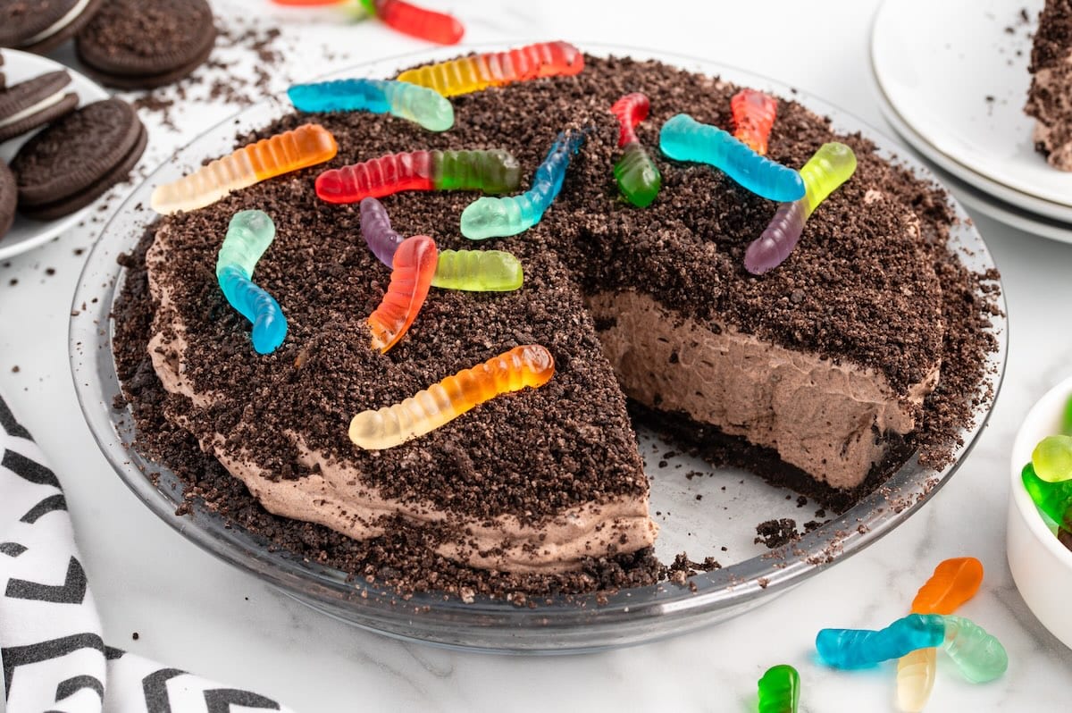 Dirt pie topped with crushed Oreos and gummy worms with a slice cut out.