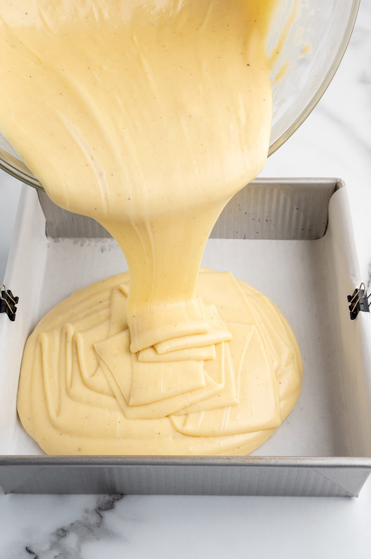 Eggnog fudge mixture being poured into a parchment-lined baking pan.