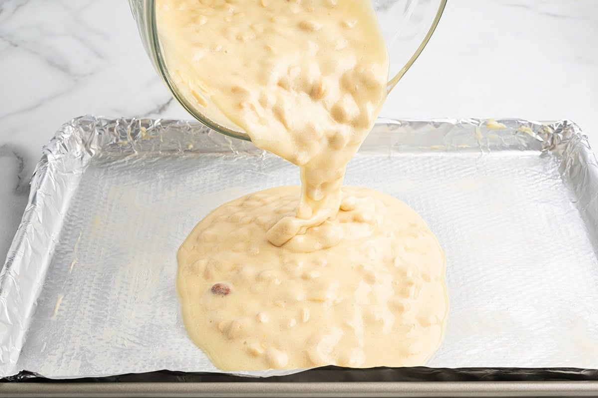 Pouring peanut brittle mixture onto a foil-lined baking sheet.