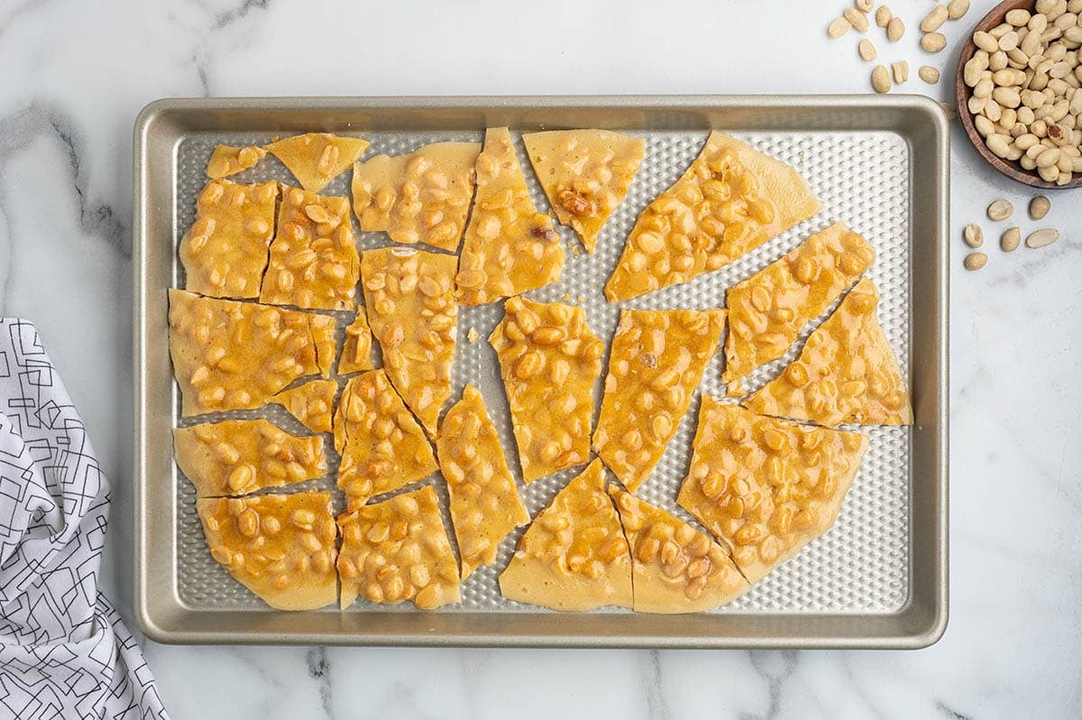 Overhead view of peanut brittle broken into pieces on a baking sheet.