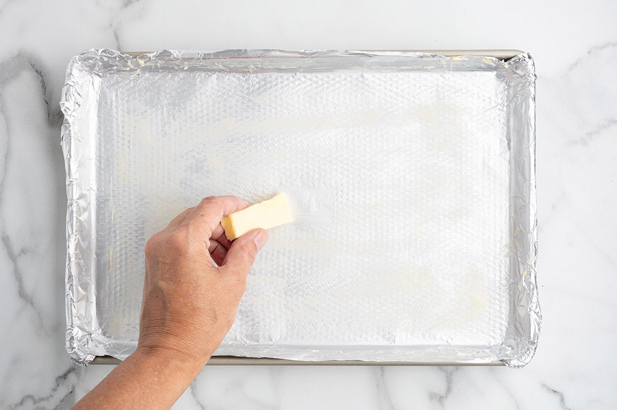 Buttering a foil-lined baking sheet with a stick of butter.