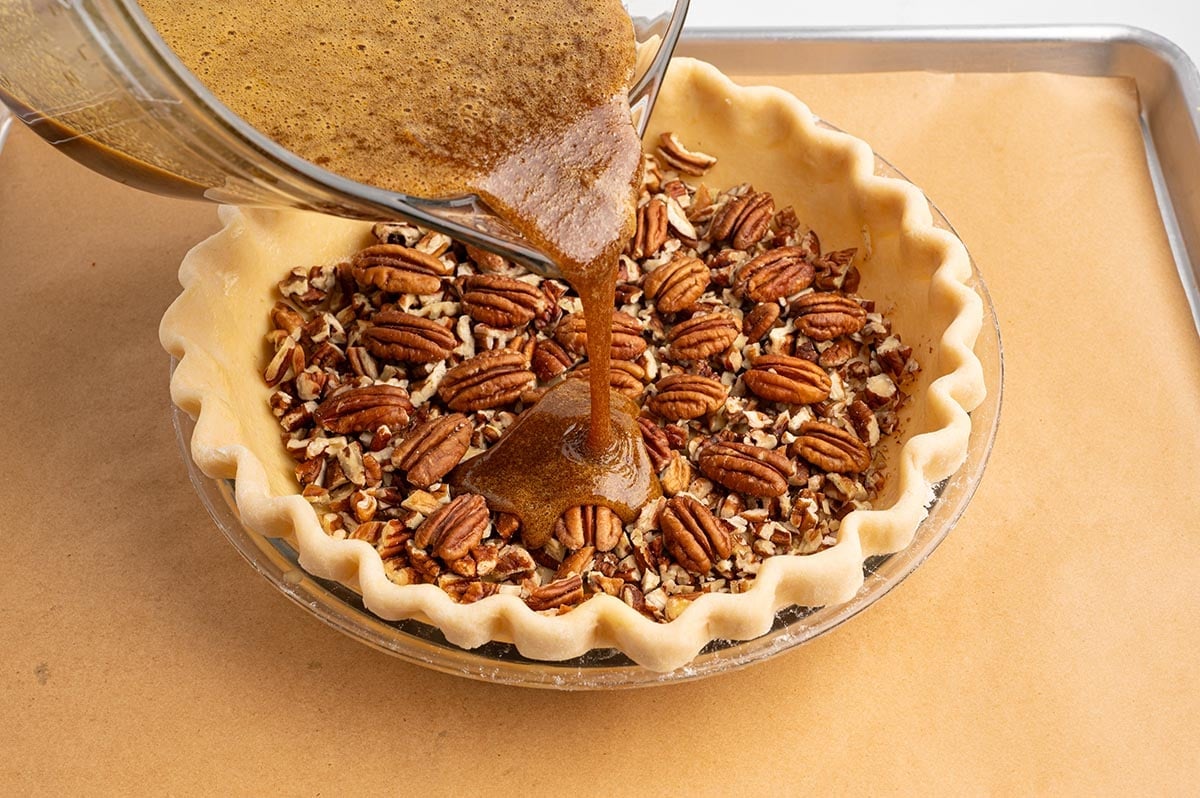 Pouring pecan pie filling over pecans in an unbaked pie crust.