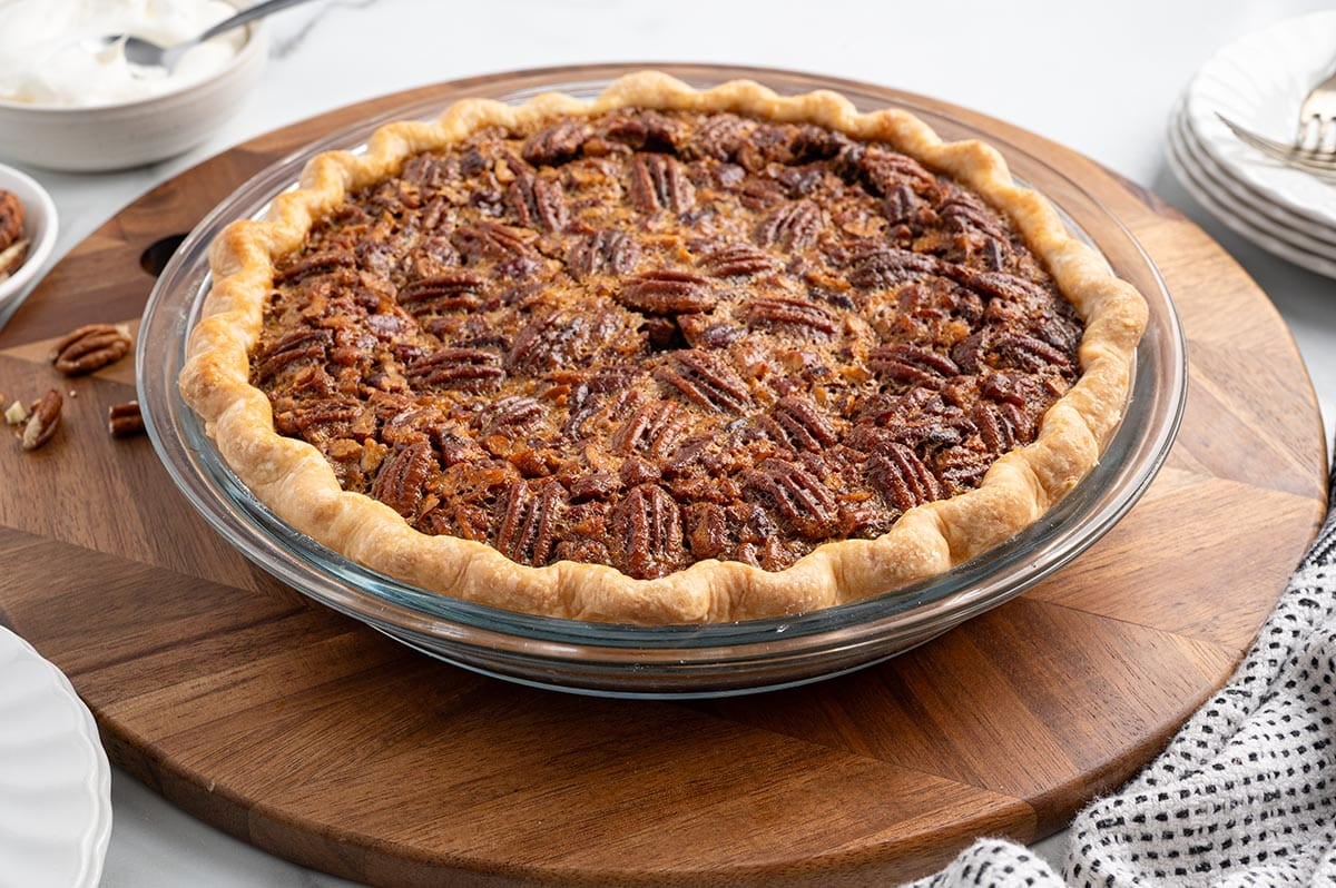 Whole pecan pie with flaky golden crust on a wooden serving board.
