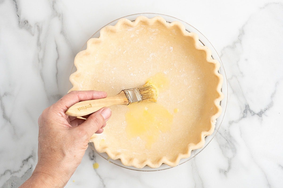 Brushing egg wash onto unbaked pie crust with a pastry brush.