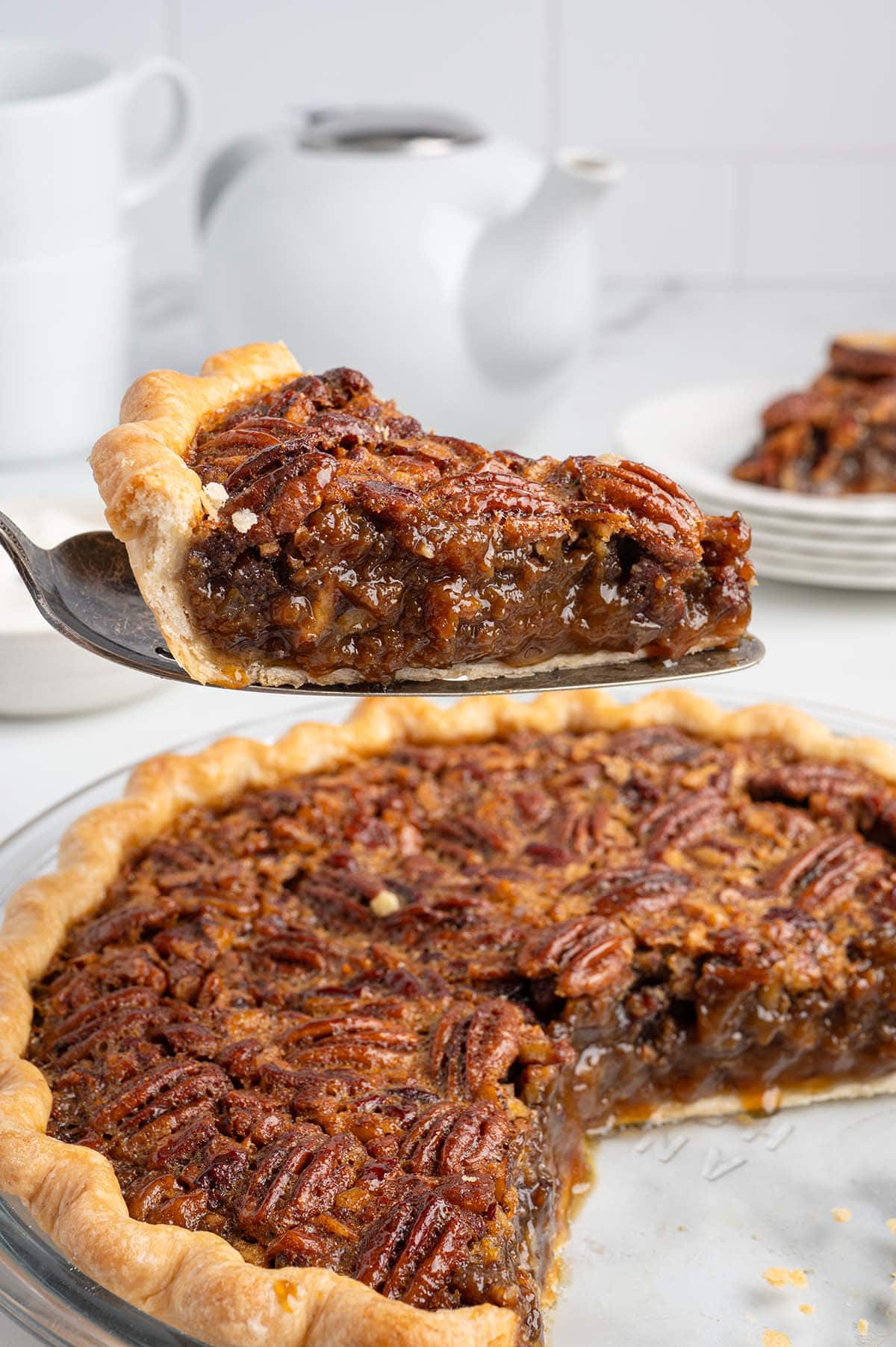 Slice of pecan pie lifted from the pie showing gooey caramel filling and pecan topping.