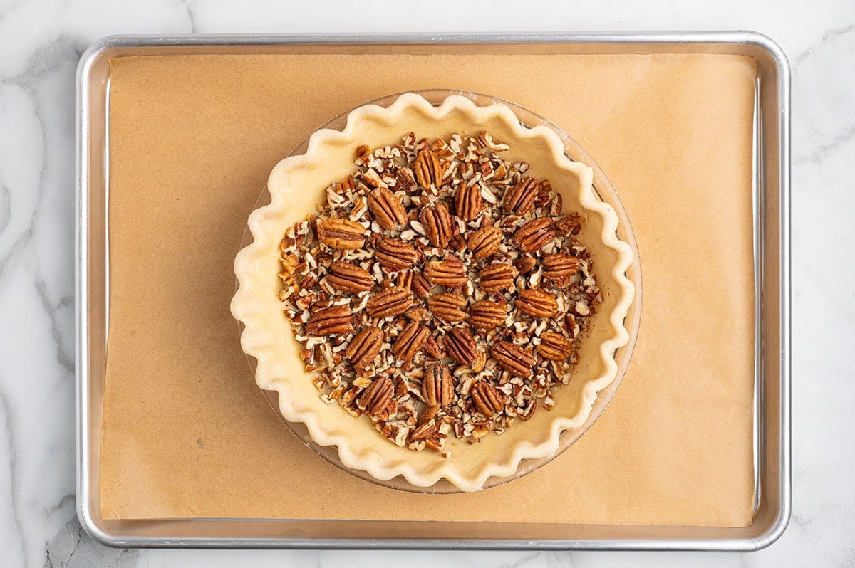 Pie crust filled with chopped pecans arranged on a baking sheet.