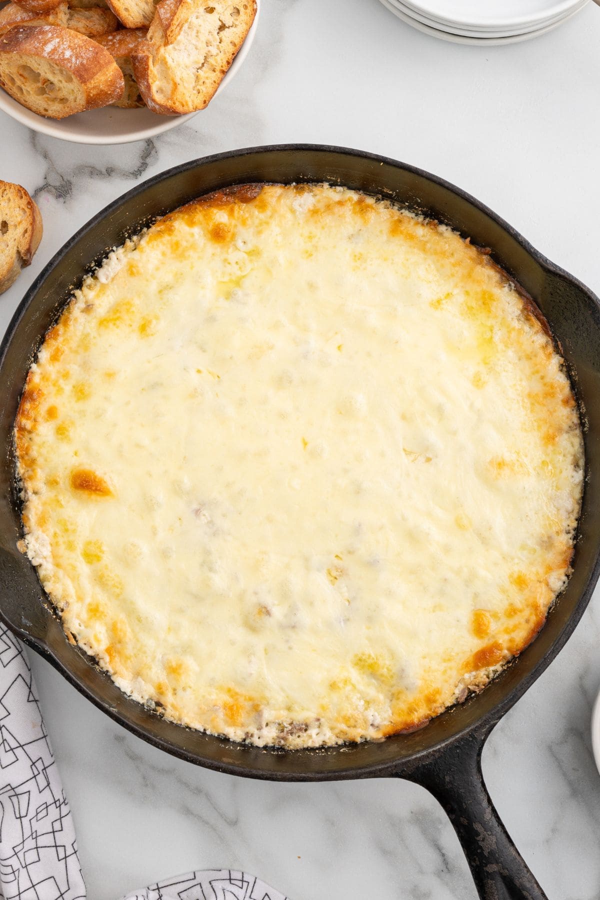 Baked Philly cheesesteak dip with melted cheese in a cast iron skillet served with toasted bread.