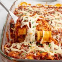 Spoon lifting cheesy ravioli lasagna with melted mozzarella and marinara sauce.