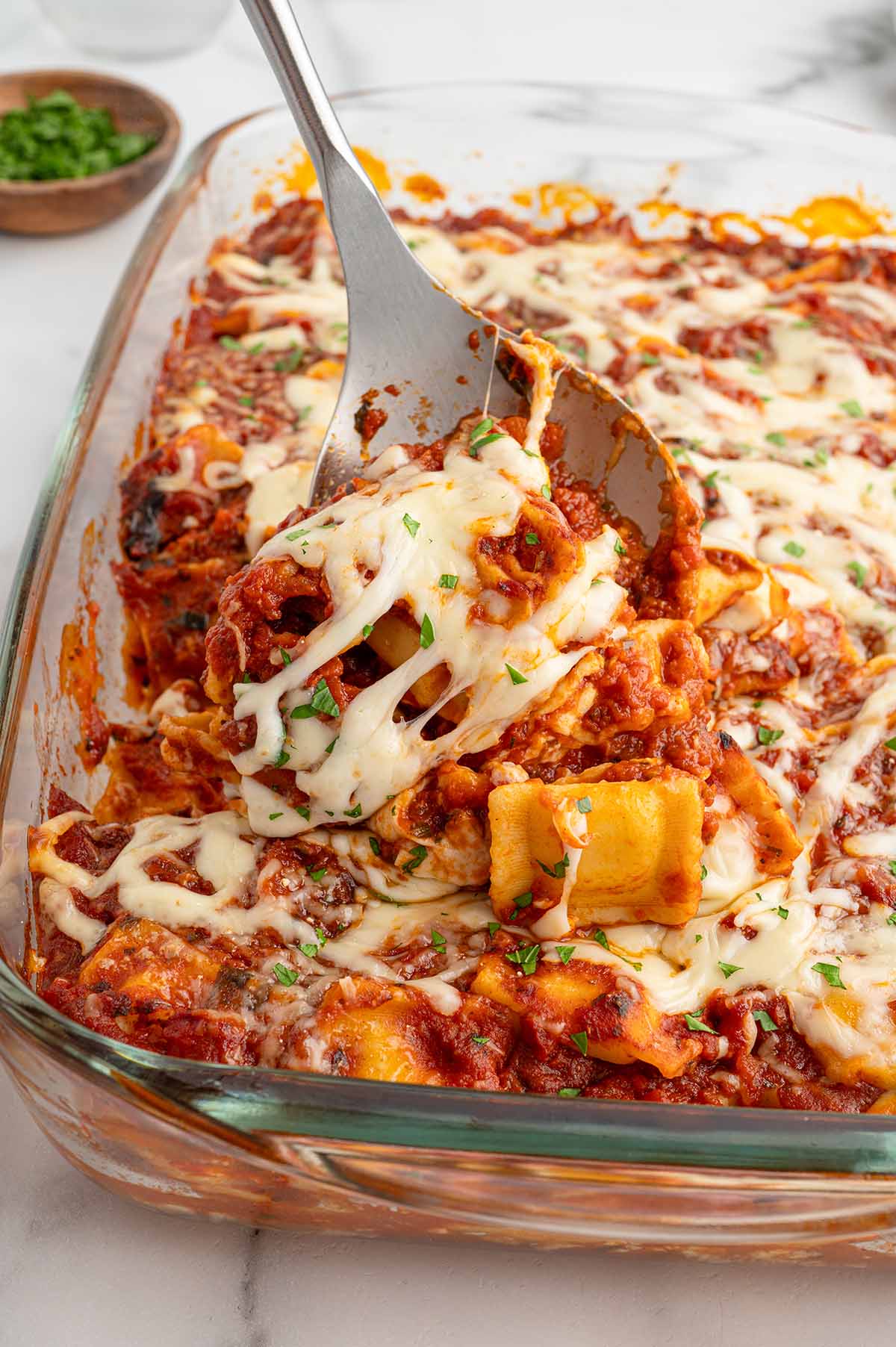 Spatula lifting a cheesy portion of baked ravioli lasagna from the dish.