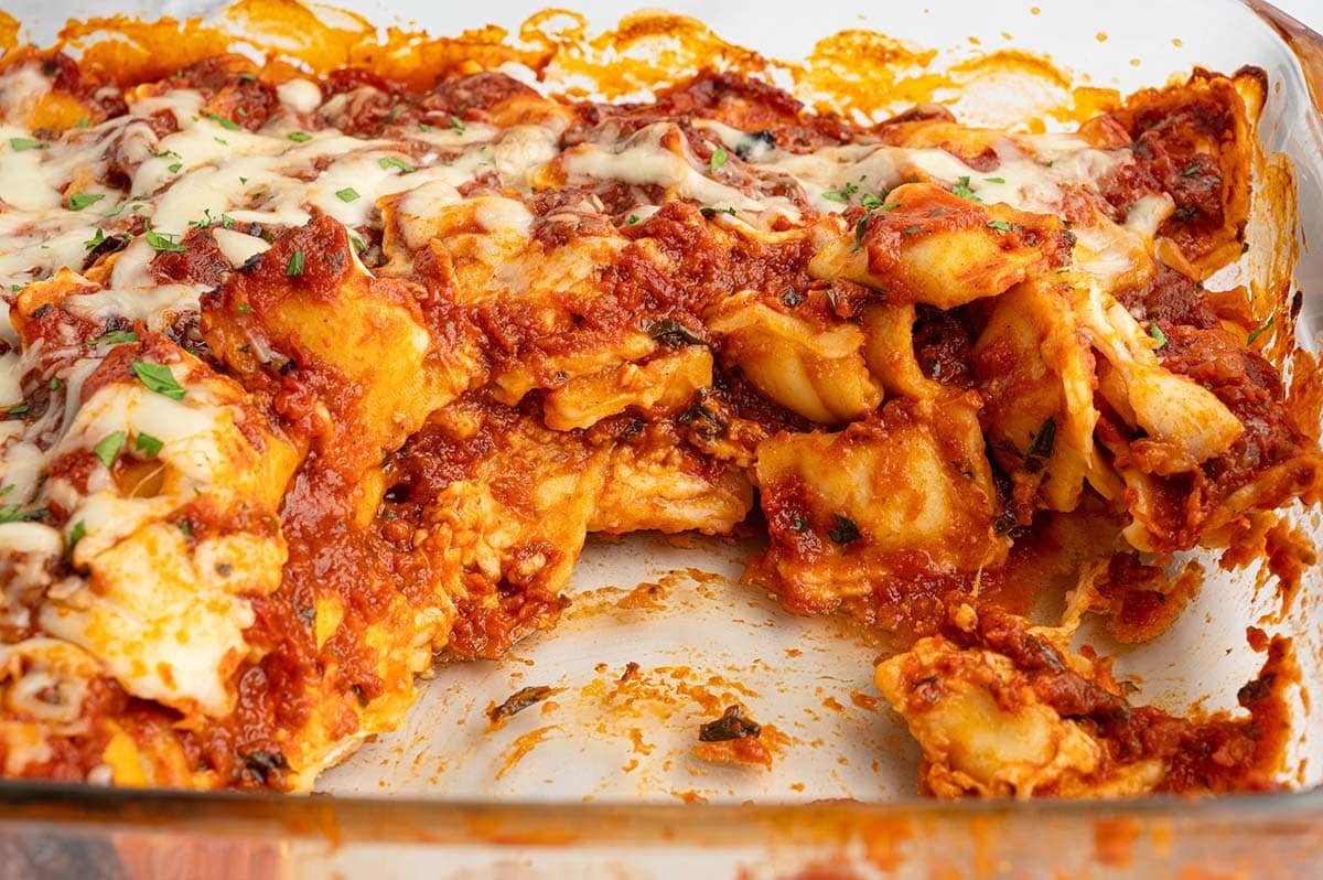 Close-up of baked ravioli lasagna with a portion removed, showing layers of pasta and sauce.
