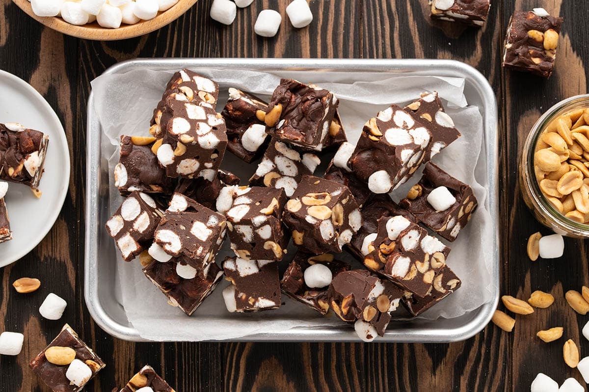 Overhead view of homemade Rocky Road Fudge squares packed with mini marshmallows and crunchy peanuts, arranged on a parchment lined tray.