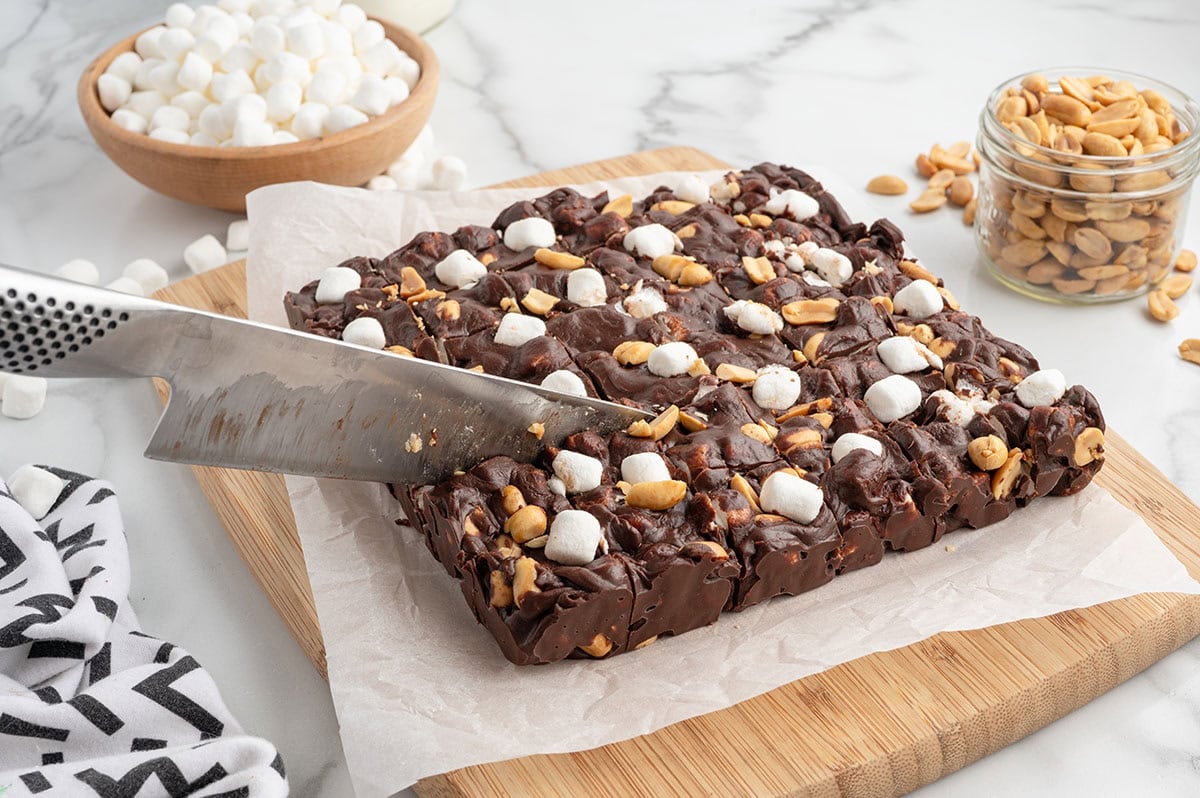 Chilled Rocky Road Fudge topped with mini marshmallows and peanuts being sliced into squares for serving.