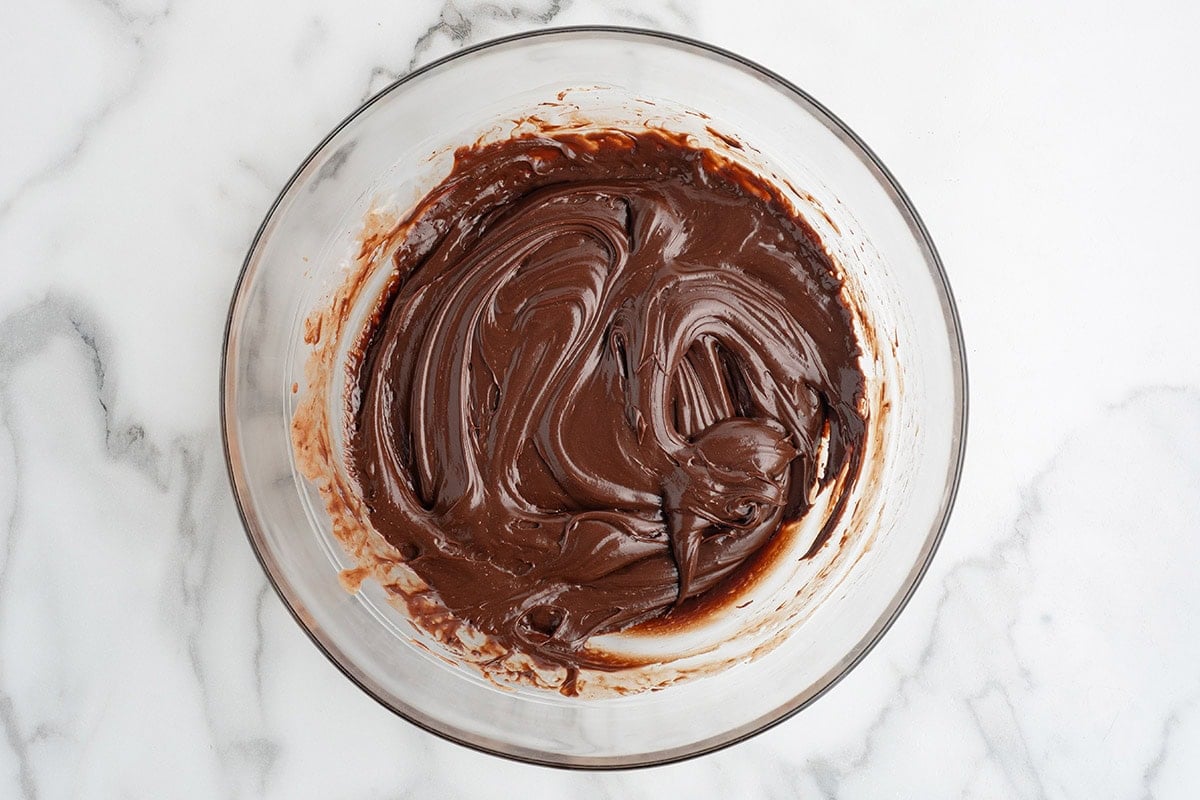 Smooth, melted chocolate fudge mixture stirred together in a glass bowl until rich and glossy.
