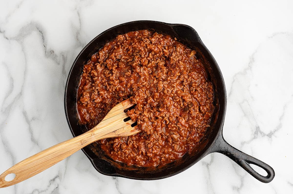Sloppy joe meat sauce in a cast iron skillet with a wooden spoon