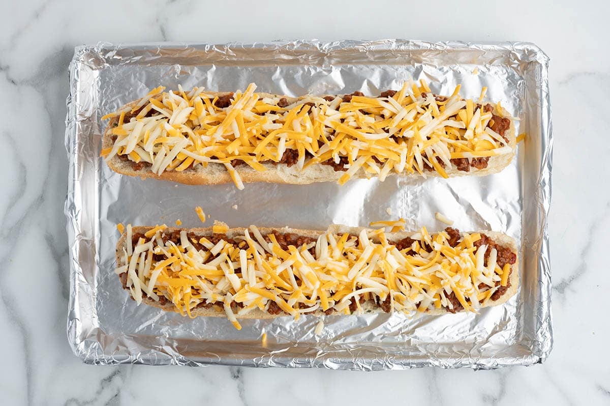 Bread halves topped with sloppy joe meat and shredded cheese before baking.