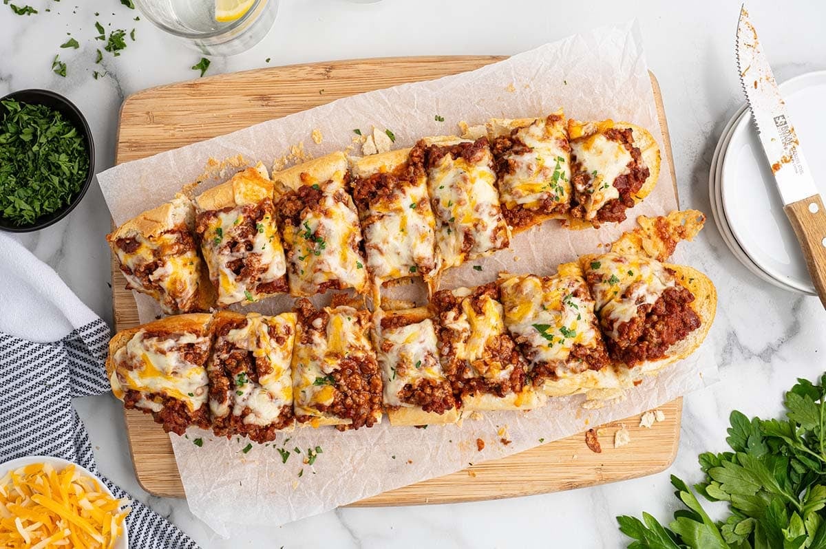 Overhead view of two split baguettes topped with cheesy sloppy joe filling on a cutting board.
