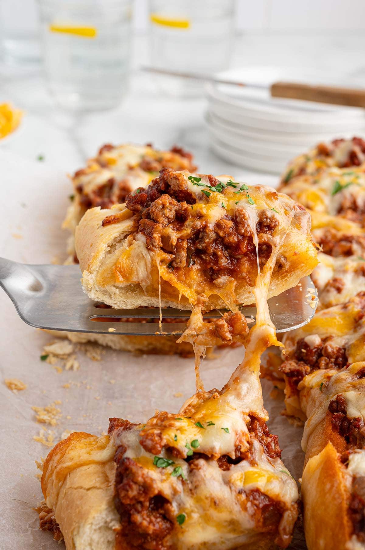 Spatula lifting a cheesy sloppy joe breadstick with melted cheese stretching underneath