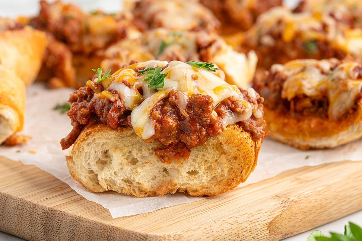 Cheesy sloppy joe breadstick topped with meat sauce and parsley on a wooden board.