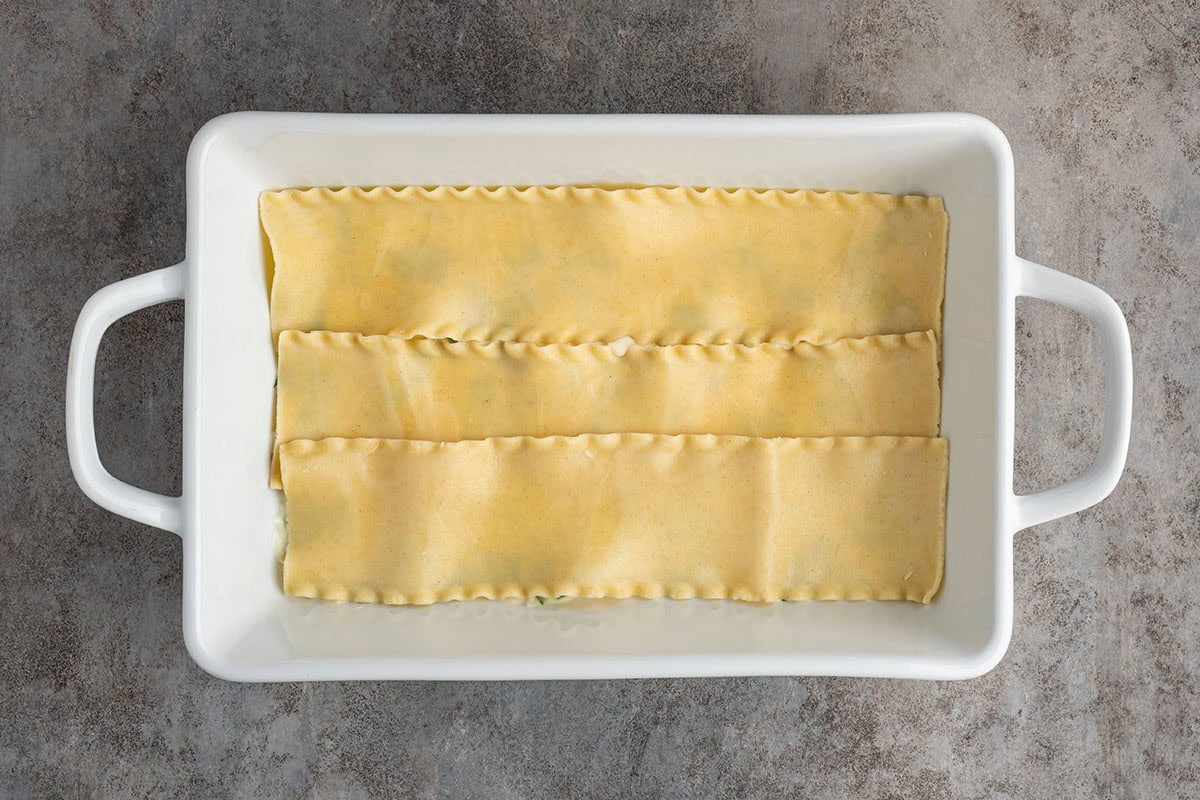 Layer cooked lasagna noodles over the filling, slightly overlapping them to completely cover the layer before adding the next ingredients.