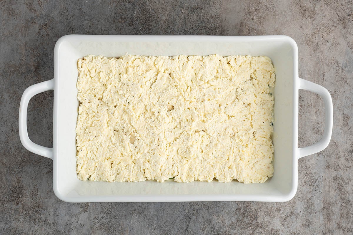 Spread the ricotta cheese mixture evenly over the lasagna noodles, covering them from edge to edge to create a smooth, even layer.