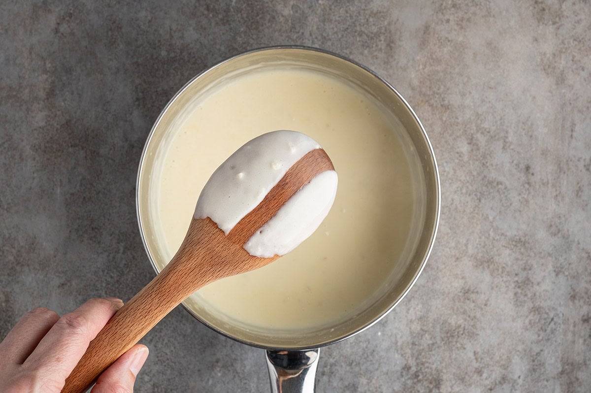Cook the creamy white sauce until it's smooth, thickened, and coats the back of a spoon before assembling the lasagna.